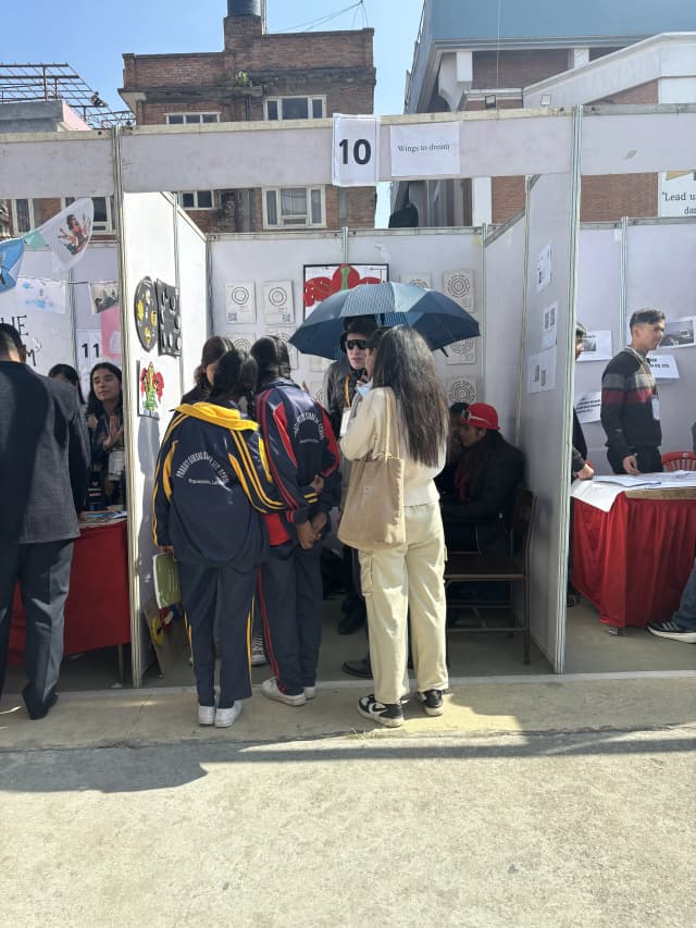 Project lead Joon Shakya explaining to the visitors at the stall. There are around 4 school students in their uniform listening to Joon.