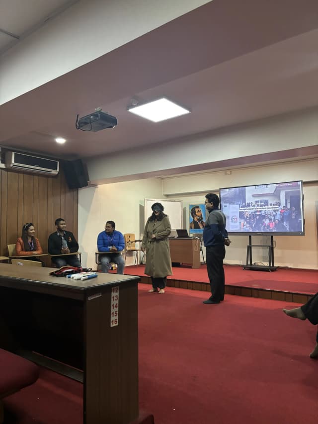 A female participant is being blindfolded and a male participant is standing beside her about to be ready for the instruction of the game. In the background Founders of CFC and Project members are observed and on the screen the website of CFC is being displayed.