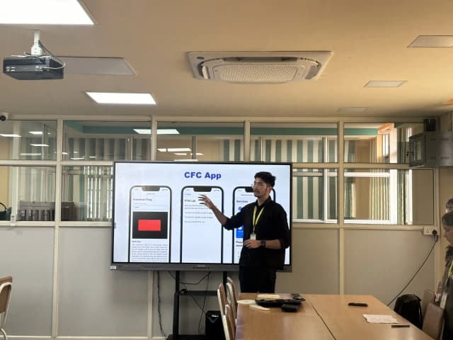 Project Secretary Karmendra Shrestha is explaining about CFC app. In the screen, CFC app is displayed on the top, 3D model of US flag is shown in left mobile screen, navigation to PTA lab in middle screen and Services just behind Karmendra.