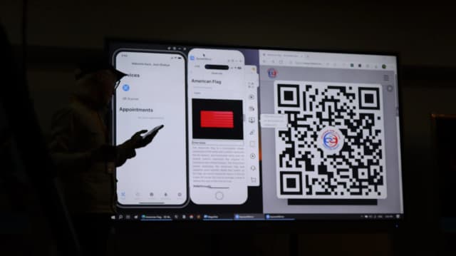 Project lead Joon Shakya is observed on the left using his phone. In the smart board, a mobile screen is displayed showing appointment section of CFC app, in another mobile screen 3D model of US flag and just beside a QR code.