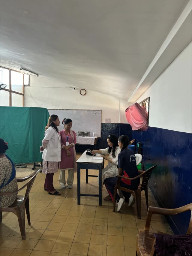 Doctor is counseling a girl student. A teacher and a girl child is also observed standing at the background.