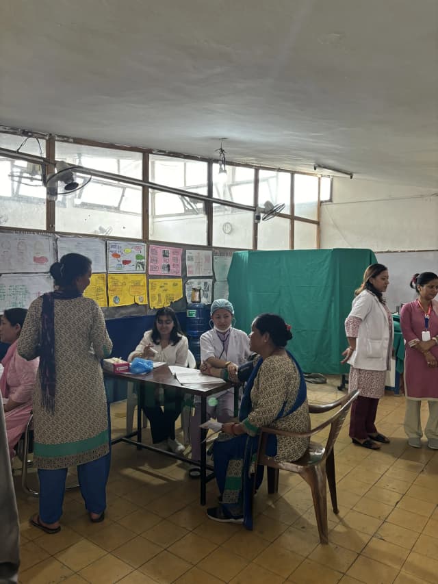 A nurse is checking the pressure of a female student. Project Member Khushi Subedi is recording the medical details.