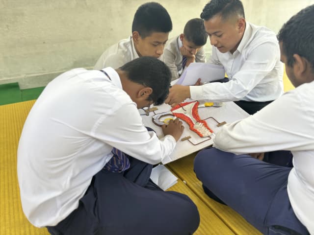 A group of male students with visual disabilities in the workshop are touching the accessible 3D model of internal female reproductive system and our project member Sambek Shahi is supporting them.