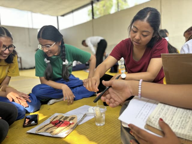 Project member Romee Jijicha Sunuwar is demonstrating a tempone by dipping it in a glass of water to the girl students with visual disabilities. An accessible 3D model of external female reproductive organ is also seen in the ground.