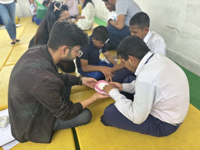 A group of male students with visual disabilities are learning the correct way of placing a pad on an innerwear and a volunteer is supporting them.