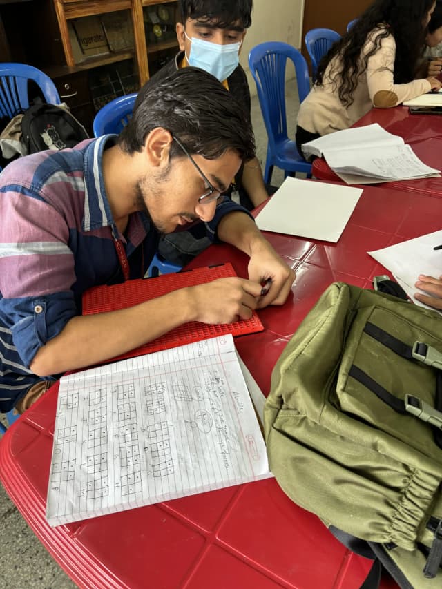 One of the project member (2024/25) Mr. Bipin Pandey writing braille using slate and stylus. He has also placed a notebook beside him.