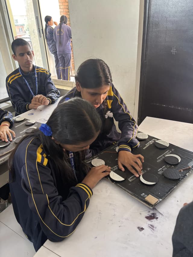 Two of the students with visual disabilities are touching the accessible 3D models of Phases of the Moon.