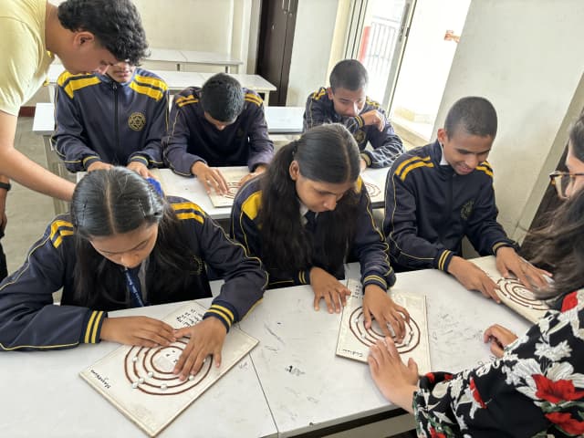 Six students with visual disabilities are touching the 3D model of atomic structures who are being seated in 2 rows of benches. Also our officer and facilitator Mr. Sangam Khadka is observed.