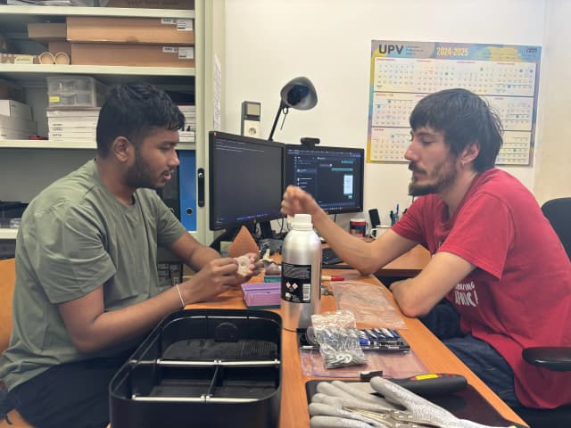 A picture taken at ETSIADI - UPV where our Founder Abhishek Shahi is touching a wheel prototype printed out from flexible resin. In the table, there are many materials placed on the office table and in background there is a computer.