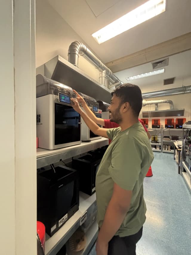 Our Founder Abhishek Shahi is exploring a 3D filament printer with his hands. In the background, there are many 3D printers placed.