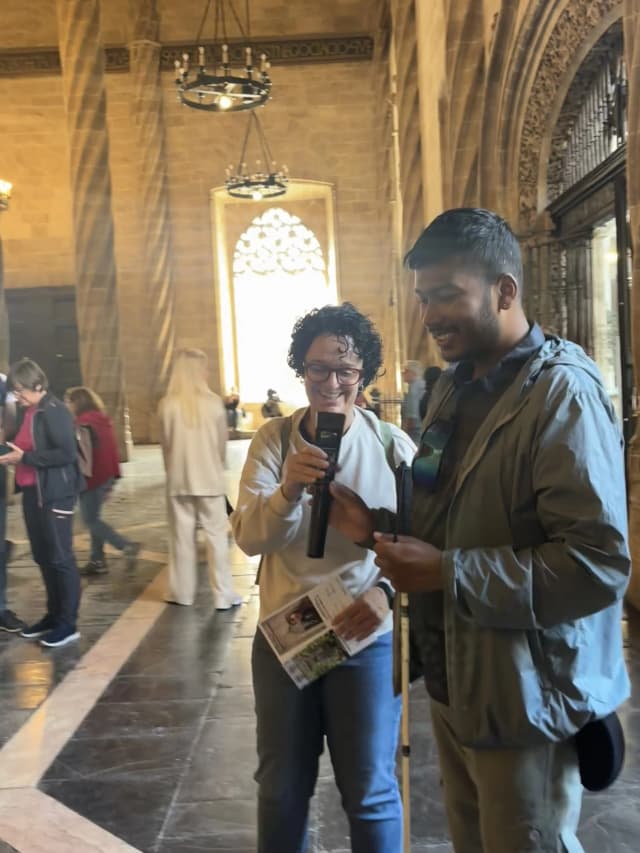 In this picture, Fanny Collado is offering an audio device to our Founder Abhishek Shahi that describes about the La Lonja. In the background, pillars of the structure can be seen along with other visitors.