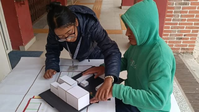 A picture of our project member, Garima Shakya supporting one of the male students with visual disability to touch the 3D model of Namuna Machindra School made out with locally available resources and giving him the orientation of different spaces.